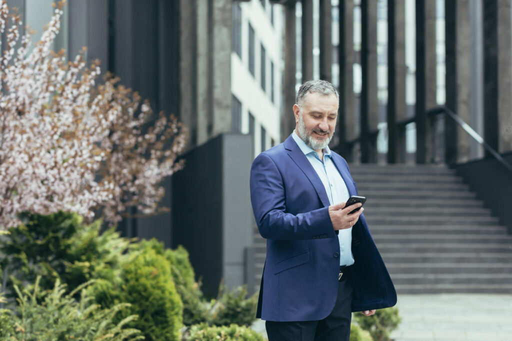 man in suit looking at cell phone outside of corporate building