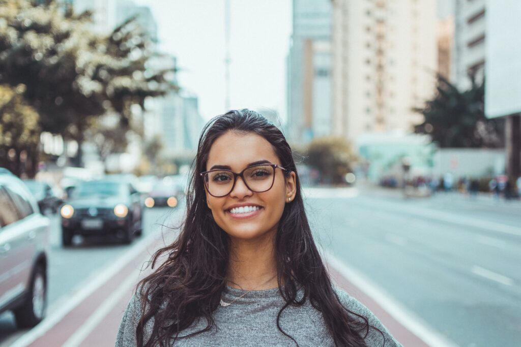young woman wearing glasses and smiling on crosswalk
